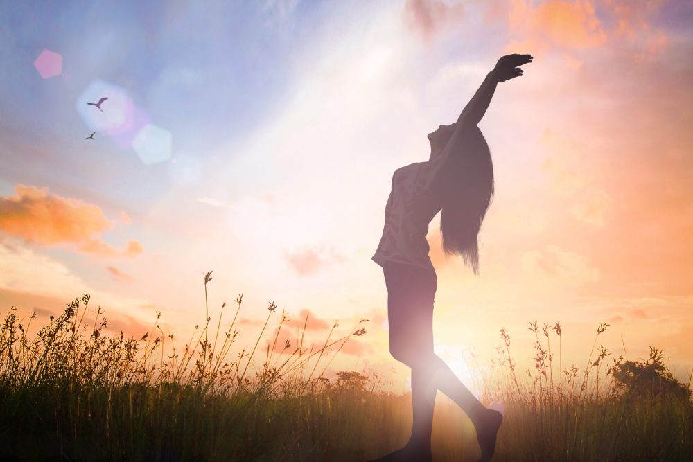 World mental health day concept: Silhouette of healthy woman raised hands for praise and worship God at autumn sunset meadow background.
