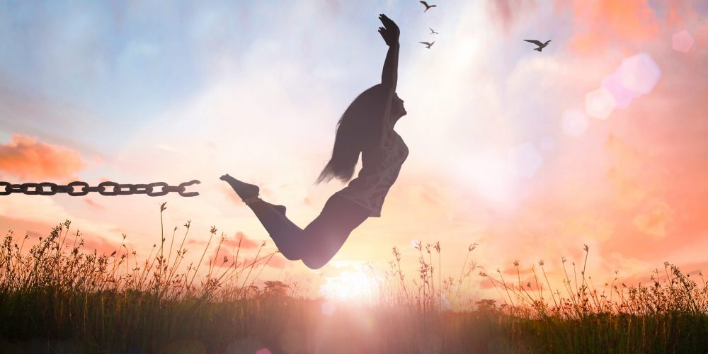 World environment day concept: Silhouette of a girl jumping and broken chains at autumn sunset meadow with her hands raised